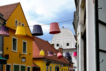 Vintage urban street in old european city with old architecture. decorative suspended large decorative lamp hoods in various colors. stucco house facades with windows. blue sky. travel and tourism.