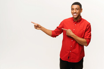 Pleasant looking curly man pointing finger aside at copy space, showing area for advertisement. Indoor studio shot isolated on white background