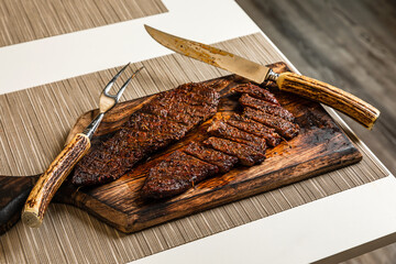 Ready to eat cooked grilled sliced piece of denver steak meat on wooden cutting board with cutlery