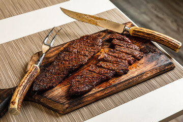 Ready to eat cooked grilled sliced piece of denver steak meat on wooden cutting board with cutlery