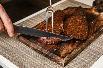 Cutting cooked grilled piece of denver steak meat on wooden cutting board with a knife - 519979039