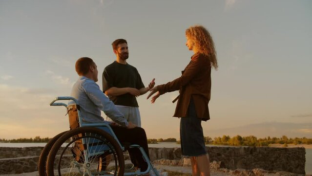young man in a wheelchair in the company of friends spend time together. A disabled person lives an ordinary life.A girl and a disabled guy spend time together on the beach