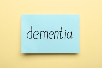 Paper note with word Dementia on beige background, top view