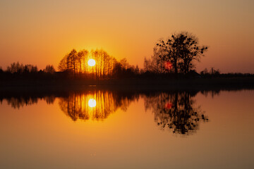 The reflection in the water of the sunset behind the trees