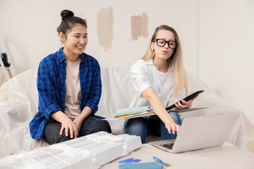 A designer girl, dressed in a white shirt and jeans, shows her client the plan of her future apartment. They are in the room where the repair is taking place. Everyone is waiting for the final result.