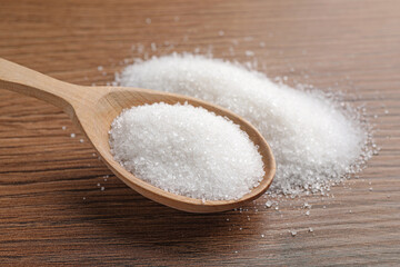 Fototapeta na wymiar Granulated sugar and spoon on wooden table, closeup