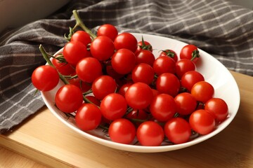 Plate of ripe whole cherry tomatoes on wooden table, closeup