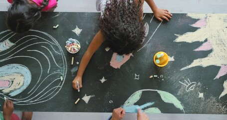 Young creative children drawing and making a colorful picture of space with chalk on a blackboard. Above view of kids coloring planets and stars. Artistic students doing a fun learning activity. - Powered by Adobe
