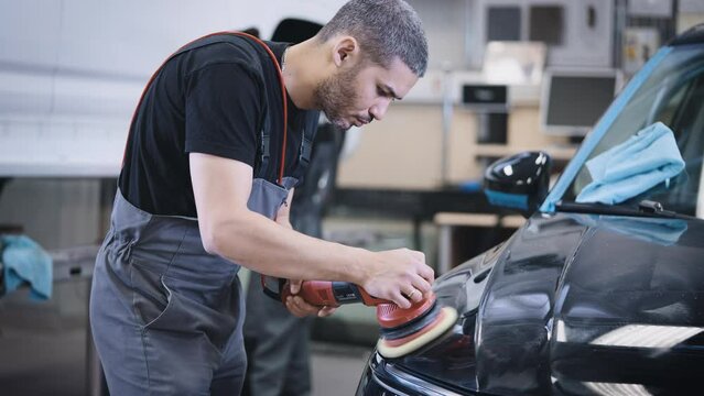 Cosmetic work with the appearance of the car. A man polishes the hood of a car in a ditying studio.