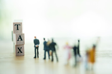 Miniature people pay queue Annual income (wood cube block with TAX text) for the year.