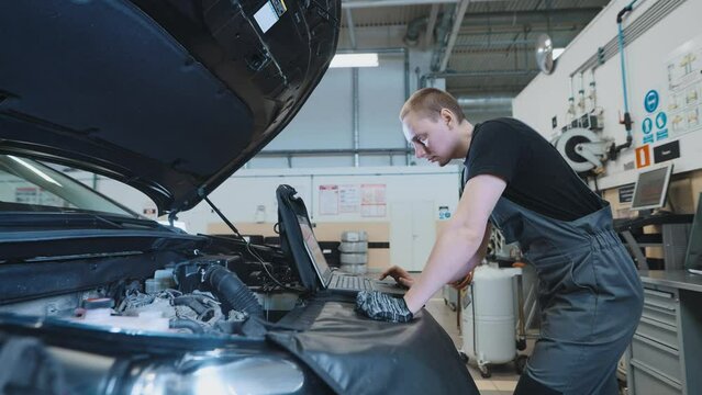 Car maintenance service. The mechanic makes diagnostics of the engine compartment using a computer.