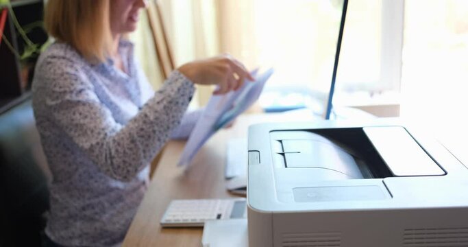 A woman sitting in the office prints out reports on the printer