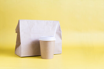 The concept of food delivery, a paper bag with food for delivery and a paper cup on a yellow background