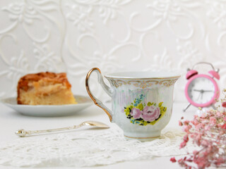 A white porcelain cup with flowers stands on a saucer. Wonderful breakfast: tea or coffee with pie.