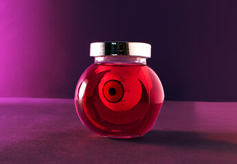 Funny eye ball in a glass jar, creative Halloween layout against purple background. Preserved food,...