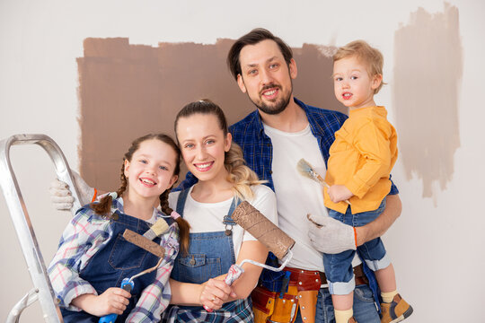 close-up of a brunette man, his blonde wife and their two children, dressed in denim, standing in their newly renovated apartment. They are hugging and snuggling together.