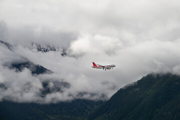Fototapeta na wymiar Airplane flying through the clouds over the pine forest covered mountains