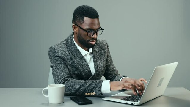 African American businessman working in the office at a laptop takes off his glasses from fatigue and is sad