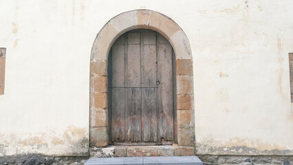 Puerta de madera en forma de arco en fachada antigua de piedra - obrazy, fototapety, plakaty
