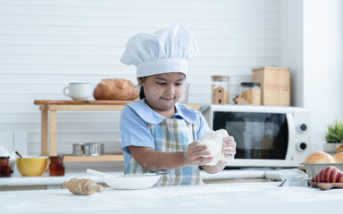 Asian little cute kid girl wear chef hat and apron with flour mess up on face and arms have fun...