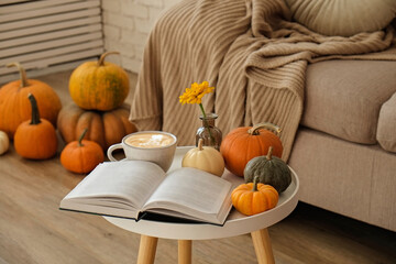 Bunch of pumpkins of different kinds, shapes and colors on the floor and a table, open book and cup...