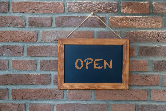 Vintage black board or school chalkboard with wooden frame and word Open isolated on brick background. Business information concept.