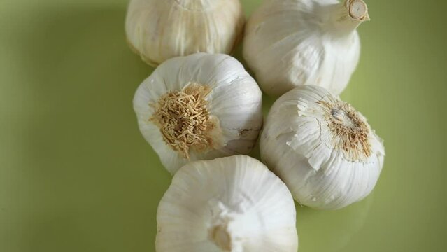 Closeup up view 4k stock video footage of several heads of garlic  spinning around isolated on green plate background. Cloves or bulbs of organic garlic