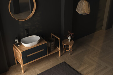Interior of modern dark bathroom with black walls, wooden floor, dry plants, arches, white sink standing on wooden countertop and a oval mirror hanging above it. 3d rendering
