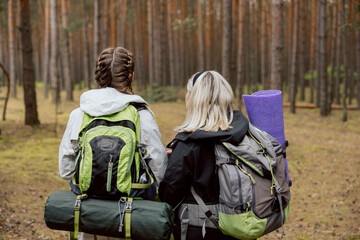 Close-up shot in the woods. Mother and daughter standing back to the camera holding backpack and...