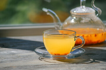 Sea buckthorn tea in glass cups and teapot on a wooden windowsill. Healthy vitamin drink
