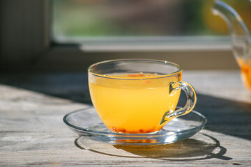 Sea buckthorn tea in a glass cup on a wooden windowsill. Healthy vitamin drink