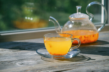 Sea buckthorn tea in glass cups and teapot on a wooden windowsill. Healthy vitamin drink