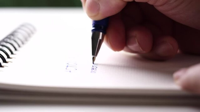 Concept of writing on paper, letter, pen, notepad, diary. Close up hand writing paper on notebook with blue pen to note, memo, list action plan at office or home desk, selective focus 4k resolution.