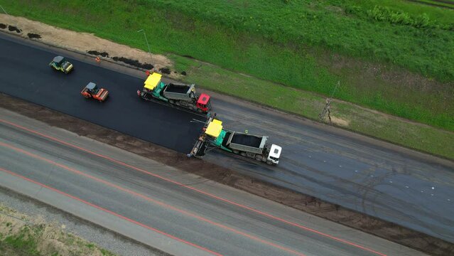 Road construction works aerial view. Laying of new asphalt on the road. The paver lays fresh asphalt, road rollers level and compact asphalt. Road construction equipment, view from a height