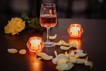 A glass of rose wine, two candles and rose petals on a dark table. Nice evening romantic atmosphere