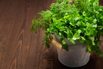 Obraz na płótnie Canvas a bunch of green dill, parsley, salad and other greens in an iron bucket, dark wooden background, concept of fresh vegetables and healthy food