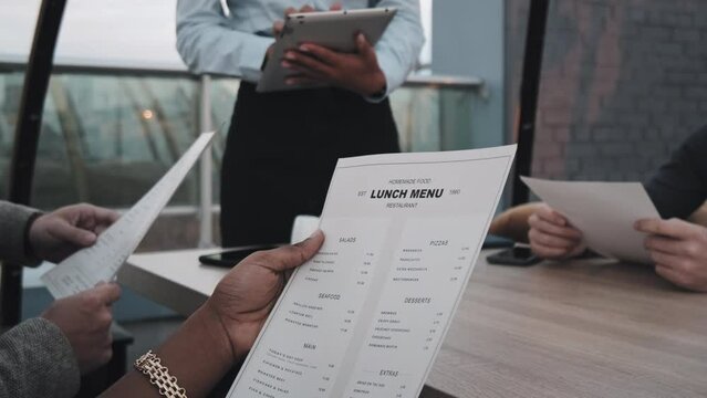 Low angle of cropped guests ordering from lunch menu in restaurant