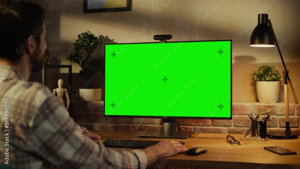 Fototapete Office Employee Working from Home, Talking on Video Call on Desktop Computer with Monitor with Green Screen Mock Up. Man Sitting in Living Room, Chatting Online with Friends and Family in the Evening.
