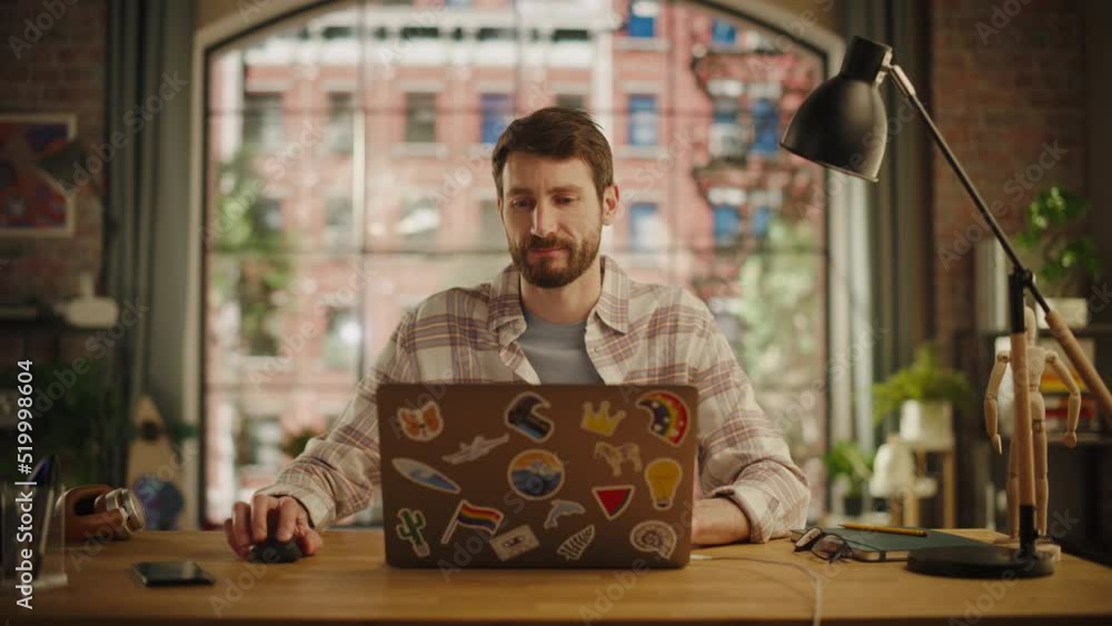Poster handsome bearded man working on laptop computer while sitting at a table in stylish cozy loft living