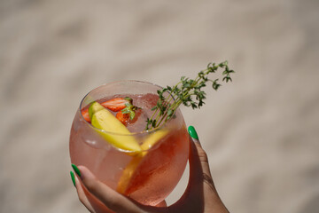 glass of gin and tonic. detail of a woman's hand holding a drink on the beach.
