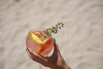 glass of gin and tonic. detail of a woman's hand holding a drink on the beach.