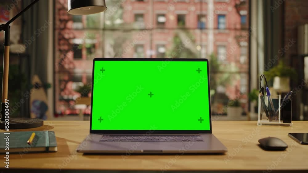 Aufkleber Laptop Computer Display with Mock Up Green Screen Standing on Wooden Table with a Notebook and Smartphone in Living Room. Chroma Key Monitor at Home or Creative Loft Office.