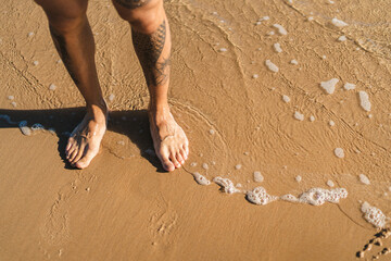 Foto detalle de unas piernas tatuadas en la playa al atardecer