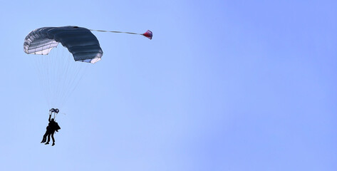 A skydiver with a white parachute canopy against a blue sky and white clouds, close-up.