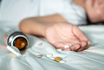 Obraz na płótnie Canvas Asian woman in white shirt is lying unconscious on a white bed after overdosing on weight loss pills, select focus on the pills to tell a story