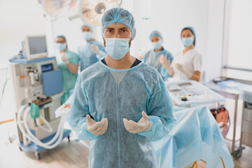 Portrait of male surgeon in mask and gloves standing in operating room, ready to work on patient