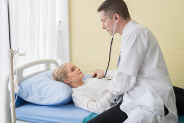 Fototapeta premium Doctor and patient at hospital. Male doctor using stethoscope examining woman patient heartbeat. Male doctor visiting and checking female patient. Health care concept