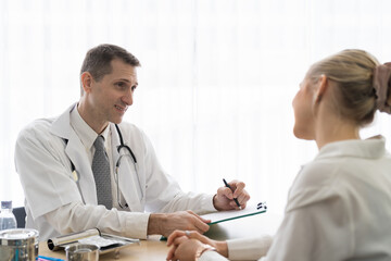 Doctor and female patient. Male doctor discussing and writing note to seek advice problems with woman patient while sitting on the table in the office at the hospital