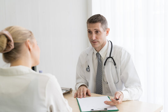 Doctor and female patient. Male doctor discussing and writing note to seek advice problems with woman patient while sitting on the table in the office at the hospital