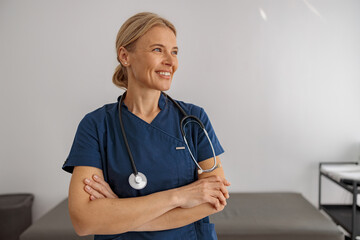 Smiling professional woman doctor with stethoscope on her workplace in hospital looking side